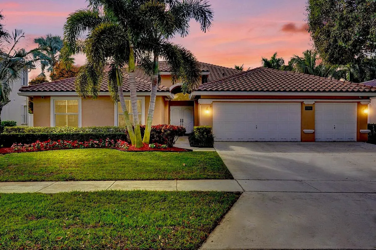 Front of the Lake Shore Village Circle home at dusk, with palm trees, flower beds and a barrel-tile roof