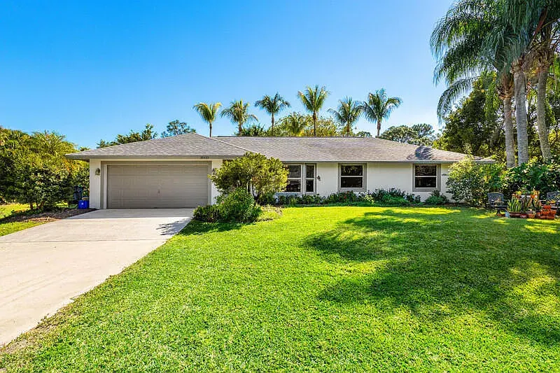 Front of the Loxahatchee home with a two-car garage, framed by palm trees and a wide lawn